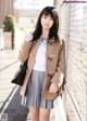 A young woman leaning against a fence wearing a coat.